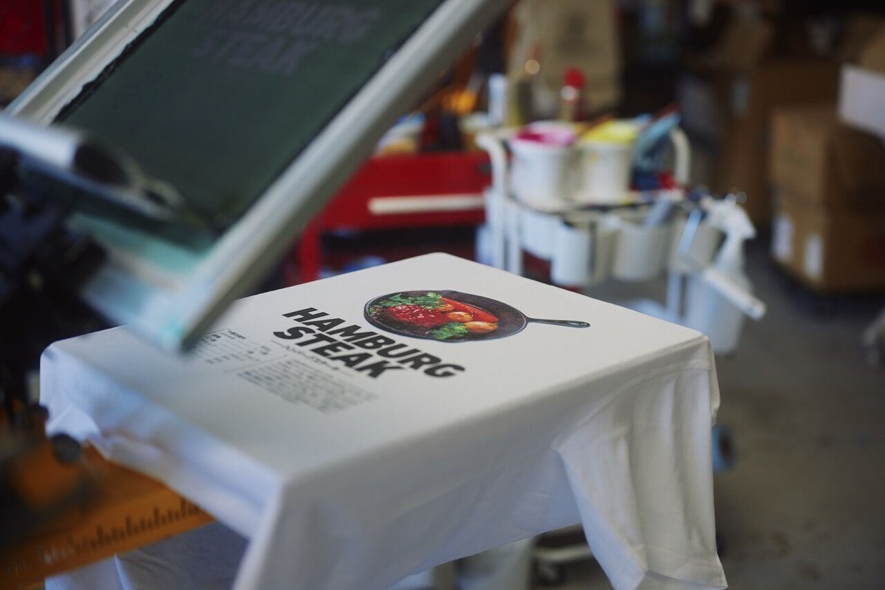 ファクトリーでフルカラースクリーンプリントプリント加工されている白いTシャツ